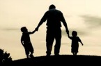 Man holding the hands of two children while walking up a hill
